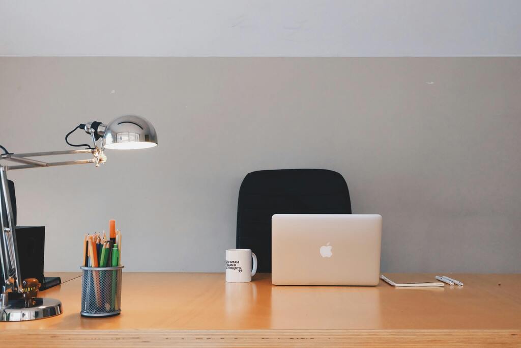 Leeg bureau met een laptop, koffie mok, pennenbakje en lamp.