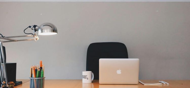Leeg bureau met een laptop, koffie mok, pennenbakje en lamp.